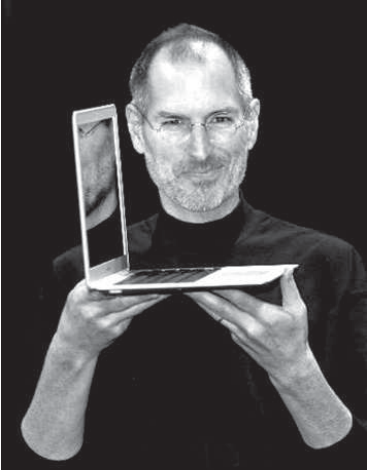 Fotografia de Steve Jobs, um dos criadores da Apple, em 2008, vestindo camisa preta e segurando à frente do corpo um notebook fino, aberto.