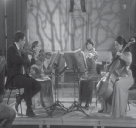 Fotografia de um quarteto de cordas com partituras em estantes: violinos, viola e violoncelo, em um salão.