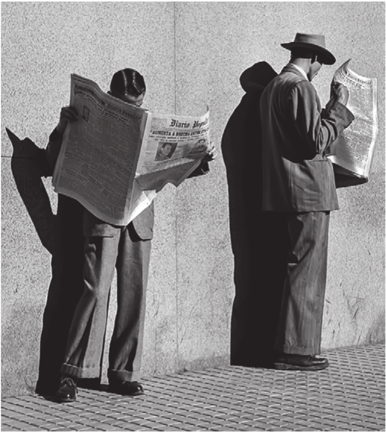 Fotografia em preto e branco. Dois homens de terno estão em pé, junto a uma parede lisa de concreto, cada um absorto na leitura de um jornal aberto diante do rosto: o da esquerda segura o Diário Popular; o da direita, de chapéu, lê um jornal dobrado. A luz do sol projeta sombras duras e nítidas dos dois na parede e no chão de lajotas limpas.