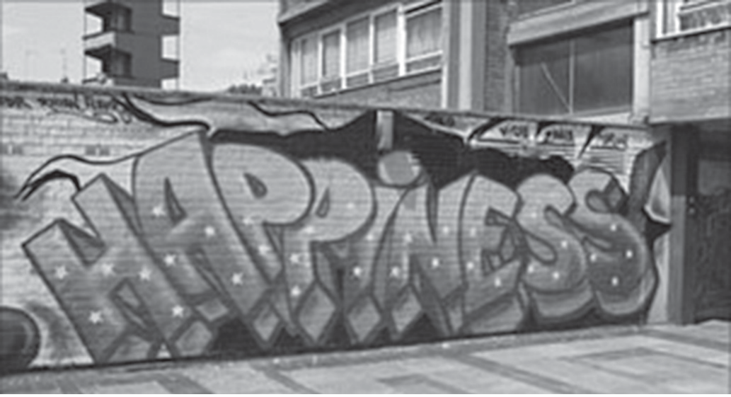 Fotografia em preto e branco de um muro urbano coberto por um grafite com a palavra "HAPPINESS" em letras grandes e estilizadas, decoradas com estrelas; ao fundo, prédios e janelas.