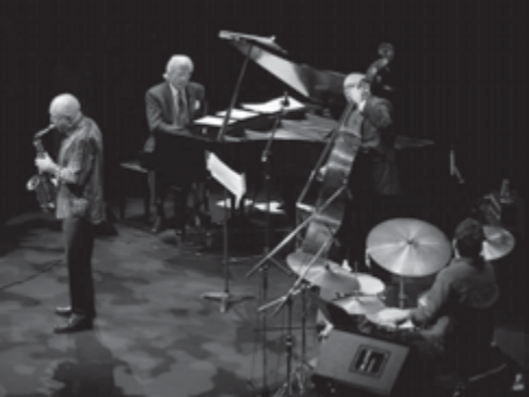 Fotografia de um grupo de jazz em palco: saxofonista em primeiro plano, pianista, contrabaixista e baterista.