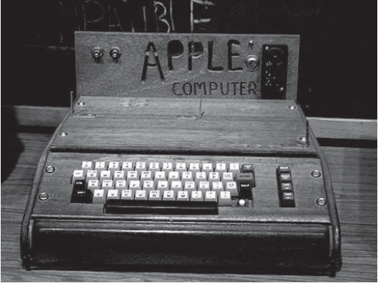 Fotografia em preto e branco do Apple-I, um dos primeiros computadores pessoais, fabricado em 1976: uma caixa de madeira com o nome "APPLE COMPUTER" no painel traseiro e um teclado de teclas quadradas na frente.