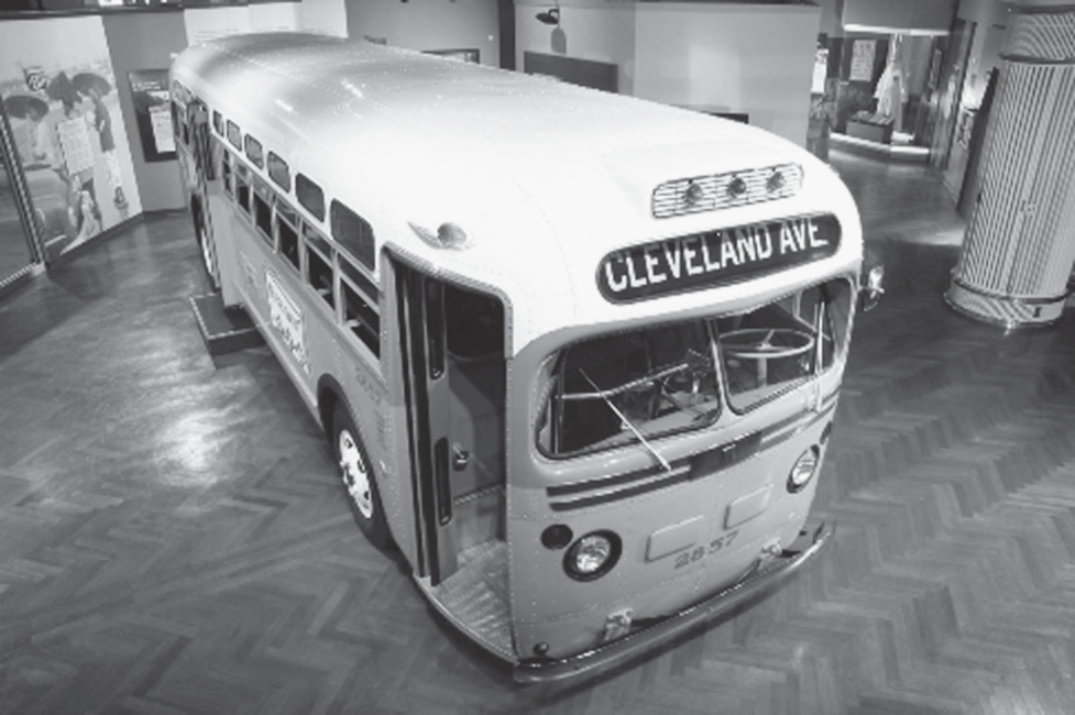 Fotografia em preto e branco de um ônibus antigo, de carroceria arredondada e faixa lateral clara, exposto no salão de um museu com piso de madeira em espinha de peixe; o letreiro frontal indica 'CLEVELAND AVE' e o número 2857 aparece na frente. Ao fundo, painéis e um pilar da exposição.