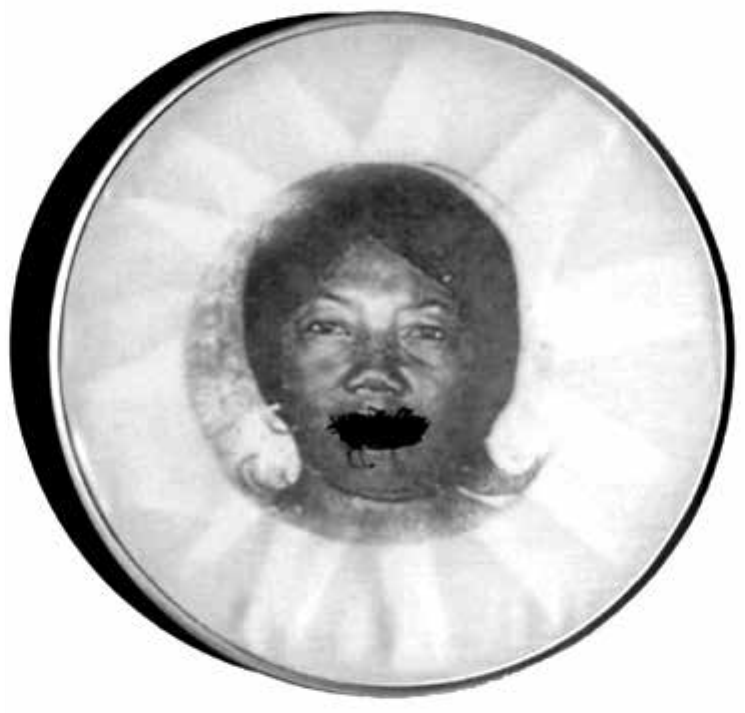 Reprodução em preto e branco de detalhe da obra Bastidores, de Rosana Paulino: um bastidor circular de madeira, do tipo usado para bordar, com tecido esticado no qual está impresso o retrato de uma mulher negra; a região da boca está coberta por um emaranhado de pontos de linha preta, como se tivesse sido costurada.