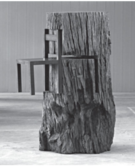Fotografia em preto e branco da escultura "Tronco com cadeira", de Nelson Leirner: um grosso tronco de árvore, com casca rugosa, em pé sobre um piso de concreto; uma cadeira de madeira simples está encaixada de lado no tronco, com o encosto e o assento saindo da superfície da madeira, como se atravessasse o tronco.