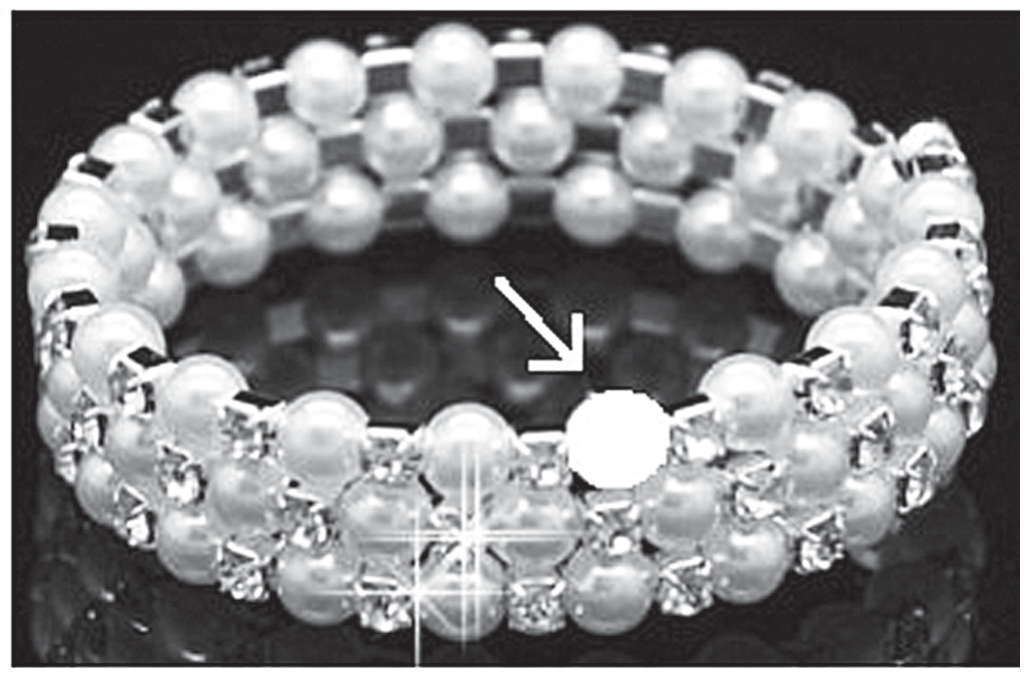 Fotografia em preto e branco de uma pulseira de pérolas esféricas em fileiras, com pequenos cristais entre elas; uma seta aponta para um espaço vazio onde falta uma pérola.