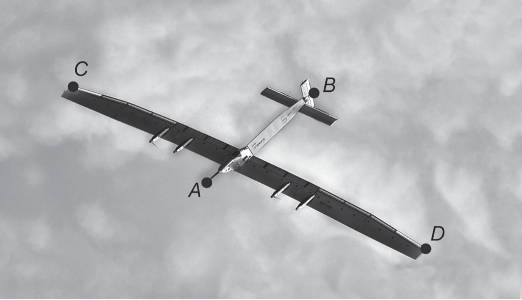 Fotografia aérea de um avião solar de asas muito longas e finas sobre nuvens; o nariz está marcado A e a cauda B (comprimento), e as pontas das asas C e D (envergadura).