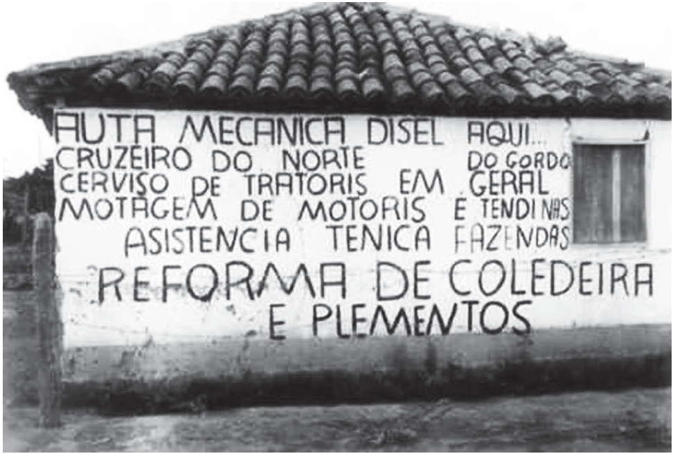 Fotografia em preto e branco da parede lateral de uma casa simples de telhado de telhas, em área rural, com uma janela à direita. Na parede, pintado à mão em letras maiúsculas irregulares, lê-se o anúncio, com a grafia original: "AUTA MECANICA DISEL AQUI... CRUZEIRO DO NORTE DO GORDO CERVISO DE TRATORIS EM GERAL MOTAGEM DE MOTORIS E TENDINAS ASISTENCIA TENICA FAZENDAS REFORMA DE COLEDEIRA E PLEMENTOS".