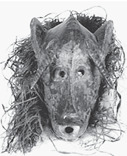Máscara senufo de madeira e fibra vegetal. Face alongada, olhos pequenos e circulares, nariz comprido, boca aberta circular e saliências laterais; fibras circundam a peça.