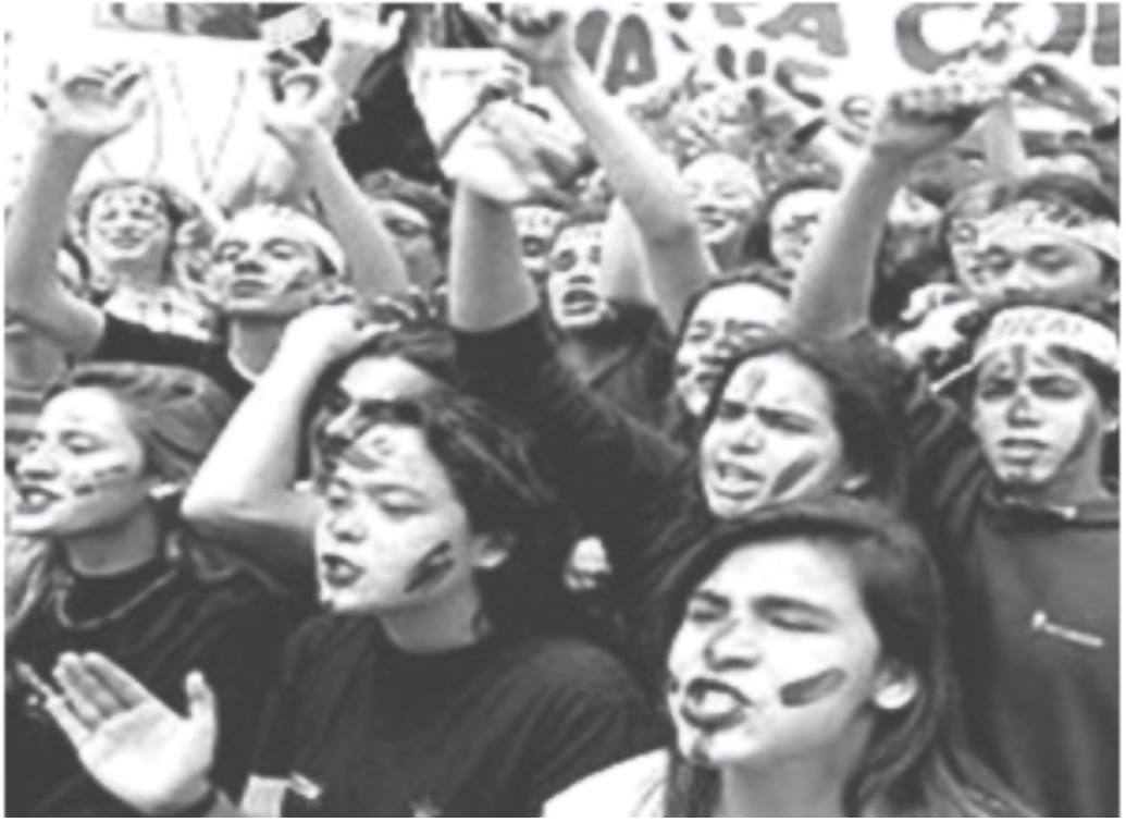 Fotografia em preto e branco de uma multidão de jovens em manifestação de rua, gritando e erguendo os braços; muitos têm o rosto pintado com faixas e alguns usam tiras amarradas na testa.