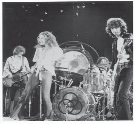 Fotografia da banda Led Zeppelin no palco: guitarrista, vocalista de cabelos longos, baterista e baixista, com amplificação.