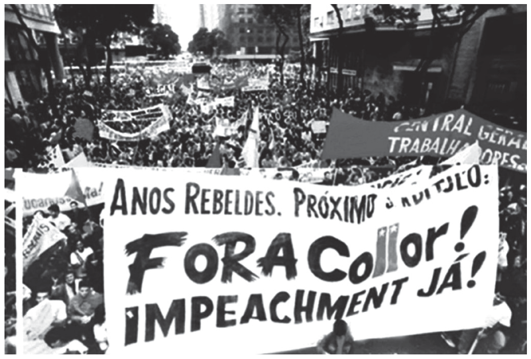 Fotografia em preto e branco de uma multidão em passeata numa avenida de cidade grande, com prédios ao fundo. Em primeiro plano, uma grande faixa branca com os dizeres "ANOS REBELDES. PRÓXIMO CAPÍTULO: FORA Collor! IMPEACHMENT JÁ!"; ao fundo, outras faixas e bandeiras, uma delas com a inscrição "Central Geral dos Trabalhadores".