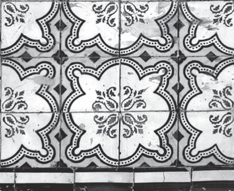 Fotografia em preto e branco de um painel de azulejos de fachada: módulos quadrados com padrão que se repete formando grandes flores de quatro pétalas recortadas, contornadas por faixas pontilhadas, com ramagens no centro e losangos nos cantos; na base, uma faixa de azulejos lisos.