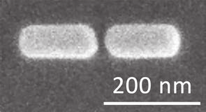 Micrografia eletrônica em tons de cinza mostrando duas nanoestruturas de forma alongada e cantos arredondados, lado a lado e separadas por um vão estreito. Na parte inferior direita, uma barra de escala branca com a indicação "200 nm".