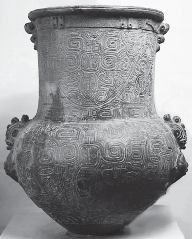 Fotografia em preto e branco de uma urna cerimonial marajoara: vaso de cerâmica com boca larga, gargalo alto e cilíndrico, corpo bojudo, pequenas alças modeladas nas laterais e toda a superfície coberta por grafismos incisos (espirais, meandros e figuras estilizadas).